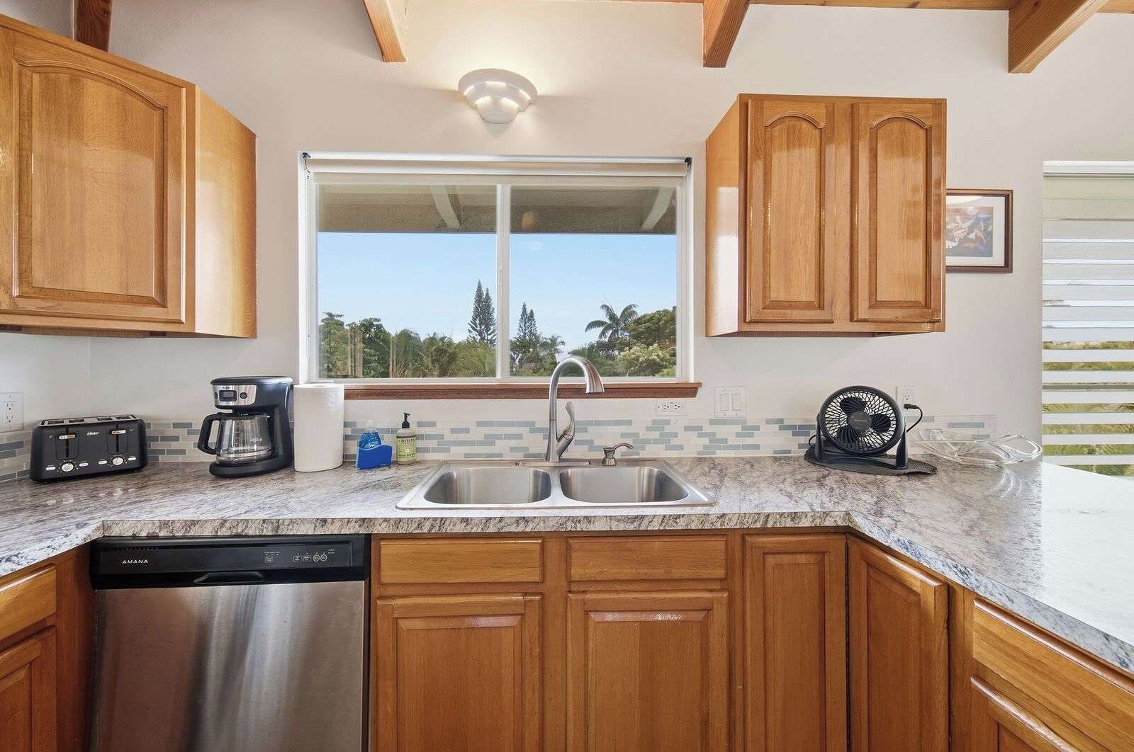 Una cocina con armarios de madera, lavavajillas de acero inoxidable, pileta doble, cafetera y ventilador.