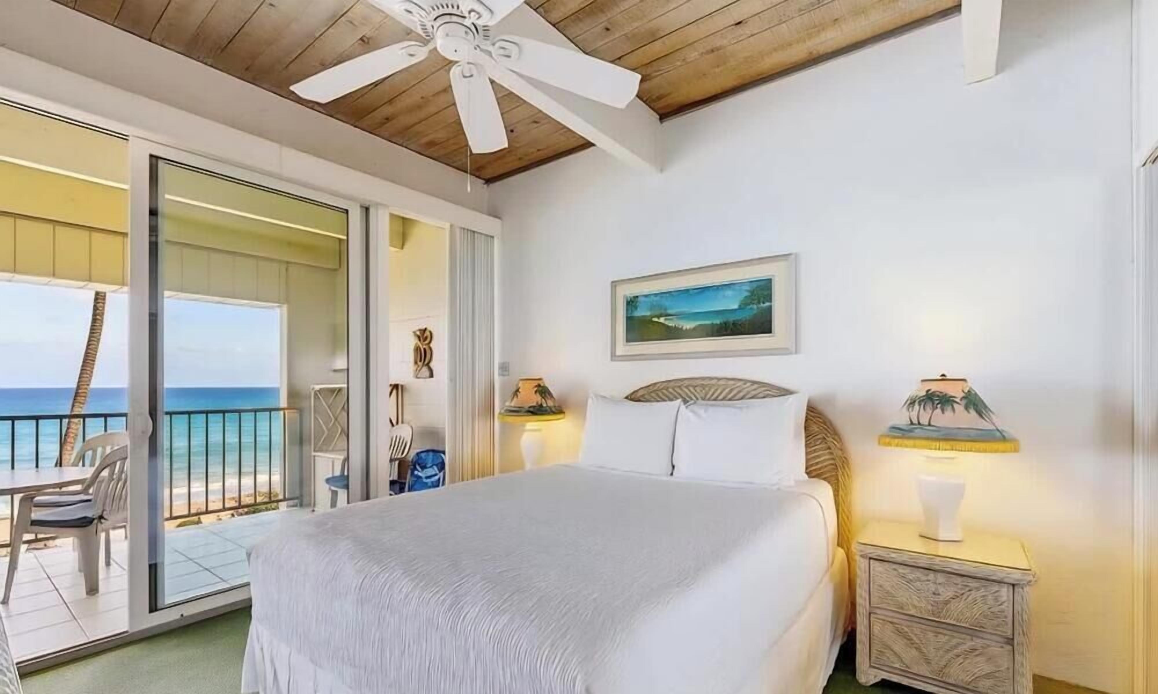 Una camera da letto con un letto, un comodino, una lampada, un quadro e vista sull'oceano.