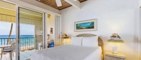 Ein Schlafzimmer mit Bett, Nachttisch, Lampe, einem Gemälde und Blick auf den Ozean.