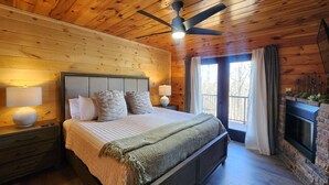 Ein Schlafzimmer mit Holzwänden, einem Bett, Nachttischen, einem Deckenventilator und einem Kamin.