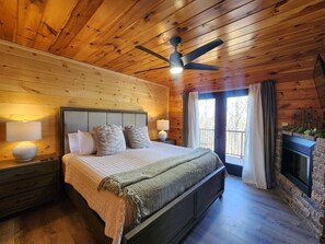 Ein Schlafzimmer mit Holzwänden, einem Bett, Nachttischen, einem Deckenventilator und einem Kamin.