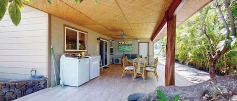 A covered outdoor area with a dining table and chairs, a washing machine, and a stone wall.