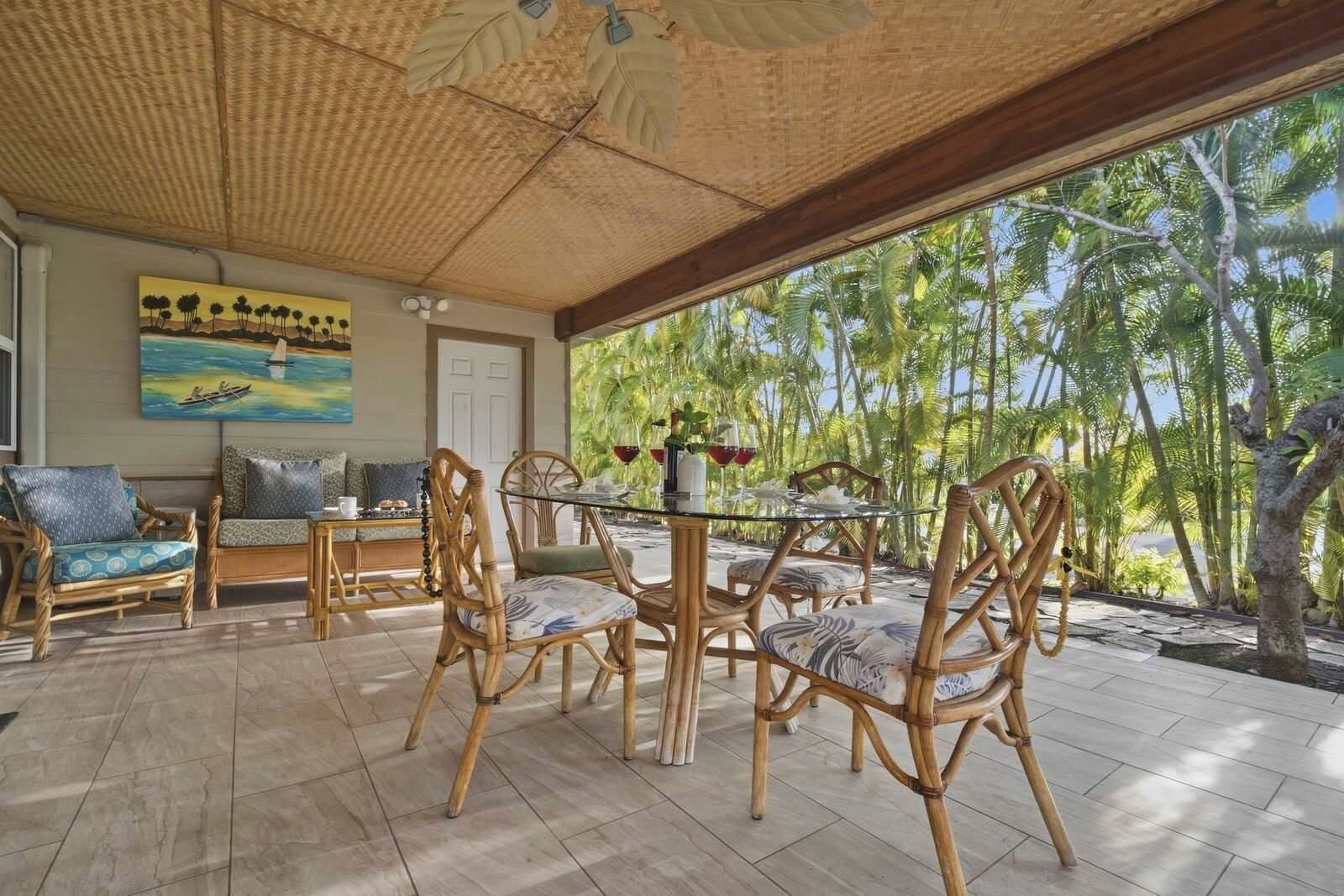 Un espace extérieur aménagé avec des meubles en osier, une table en verre et une vue sur les palmiers.