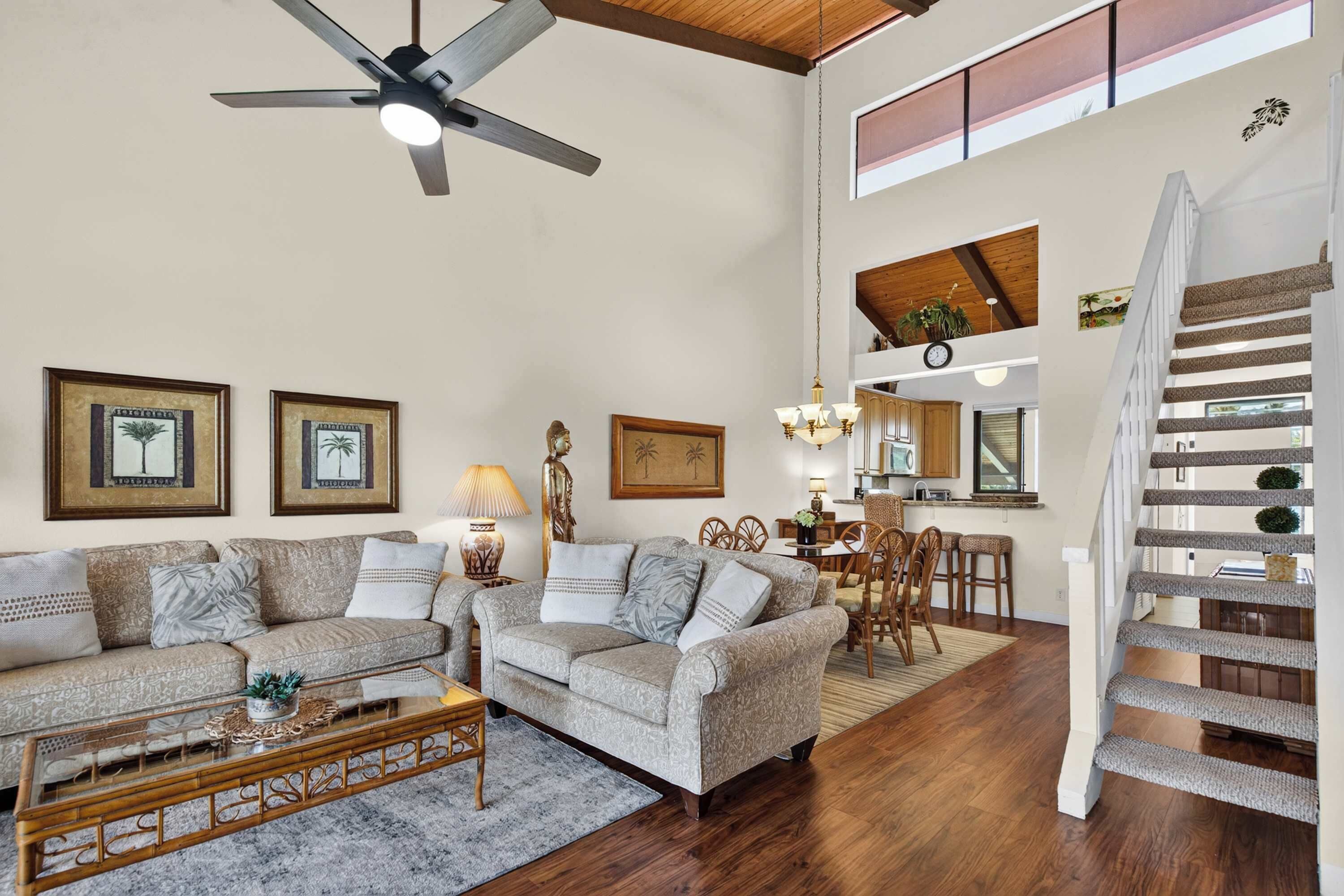A spacious living room with a high ceiling, a ceiling fan, and a staircase leading to an upper level.