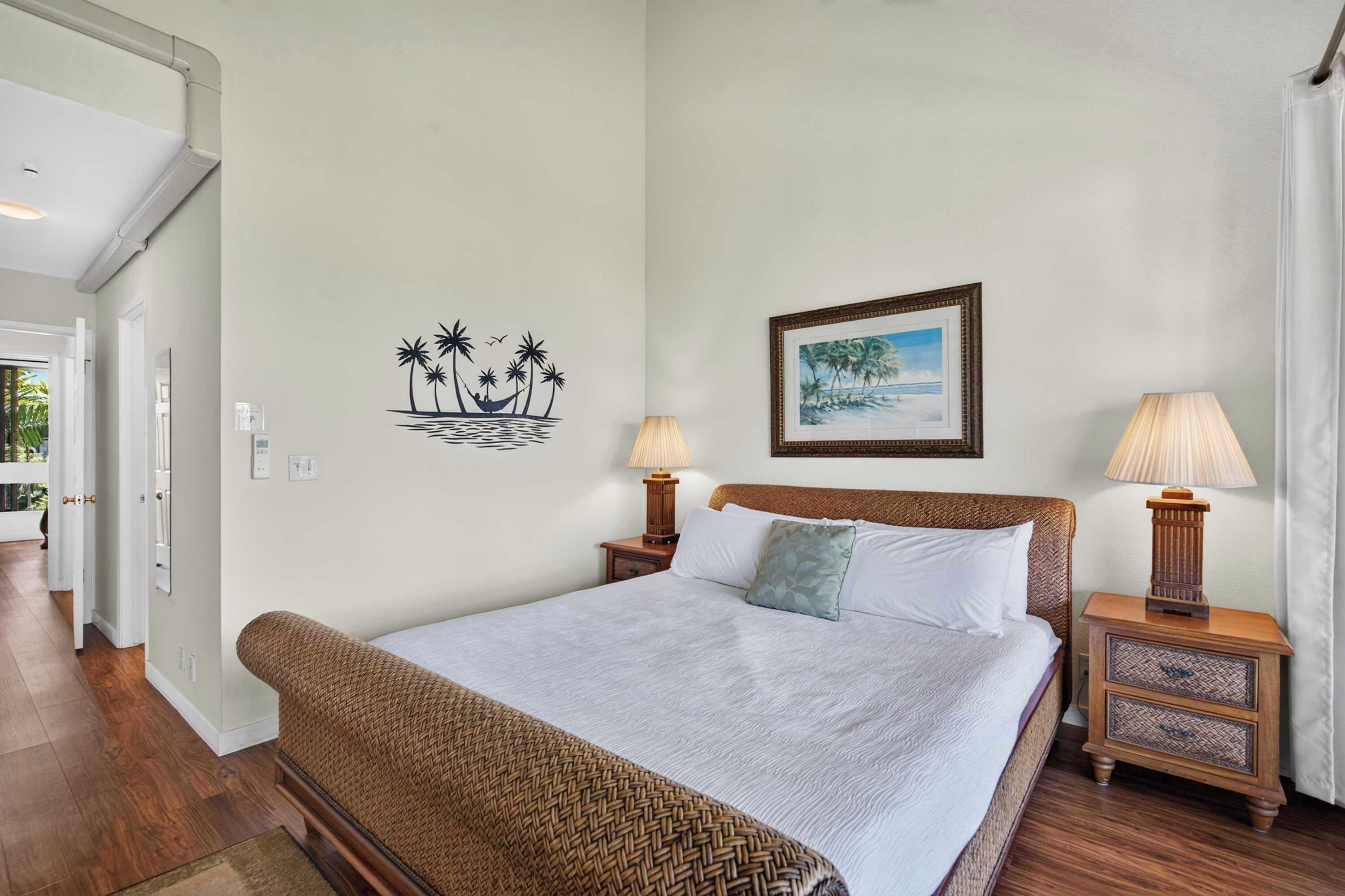 A bedroom with a bed, two nightstands, a lamp, a framed picture, and a wall decal of palm trees.
