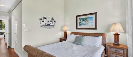 A bedroom with a bed, two nightstands, a lamp, a framed picture, and a wall decal of palm trees.
