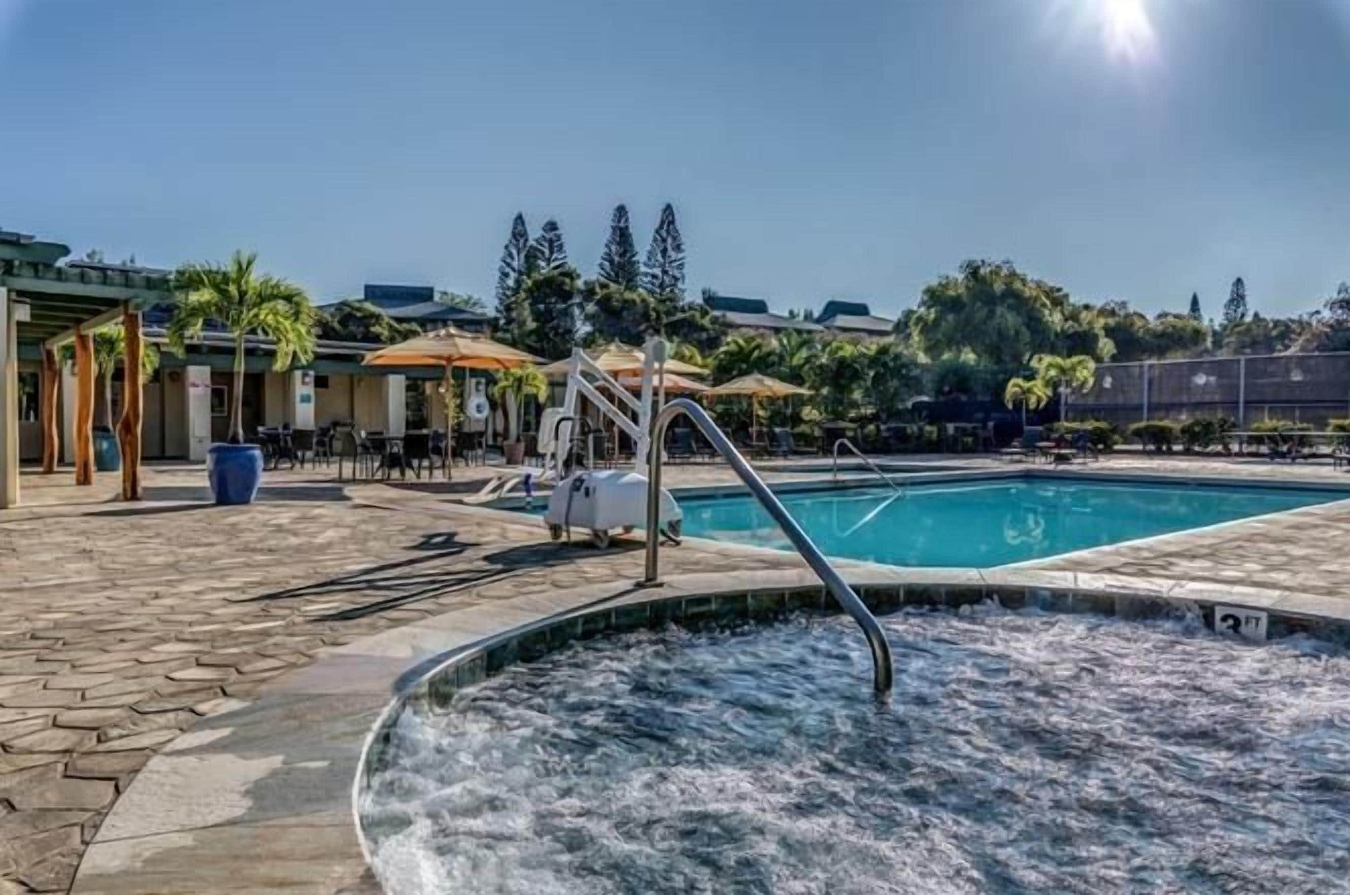 Piscina com hidromassagem, área de estar ao ar livre e espaço coberto com guarda-sóis.