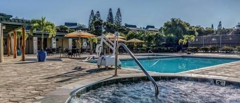 A swimming pool with a hot tub, outdoor seating, and a covered area with umbrellas.