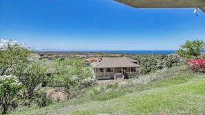 Una casa amb un teulat inclinat, envoltada de vegetació i una vista clara del mar.