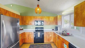 Una cocina con armarios de madera, un refrigerador de acero inoxidable, una estufa negra y una ventana con vistas.