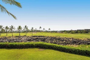 A golf course with a rocky outcrop in the foreground, palm trees, and a clear sky. - New Walk to Waikoloa Beach from a Resort-Style Condo (Waikoloa)