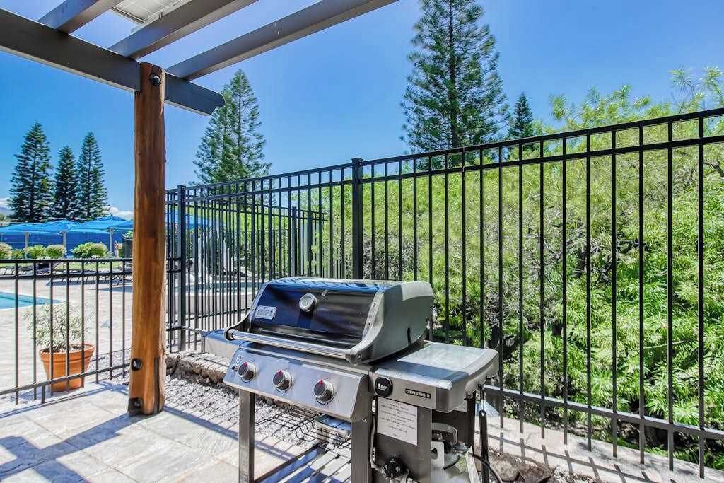 A barbecue grill on an outdoor patio with a metal fence and trees in the background.