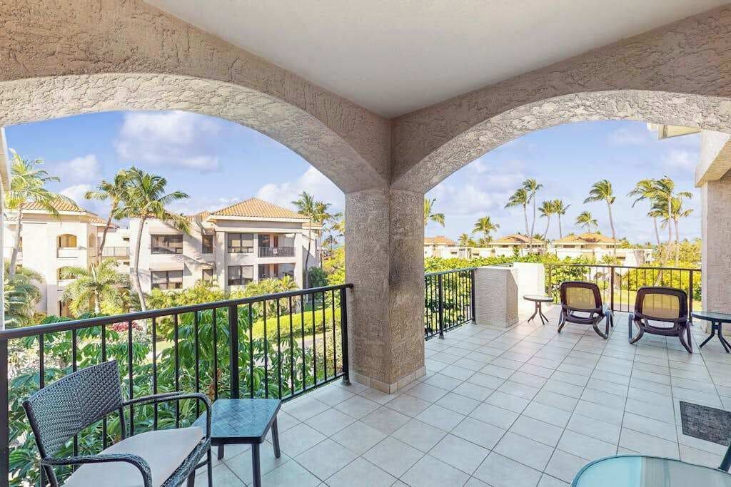 A balcony with a view of palm trees and buildings, furnished with chairs and a table.