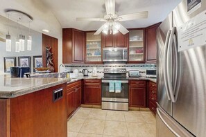 Eine Küche mit Holzschränken, Edelstahlgeräten, einem Deckenventilator und einem Kühlschrank.