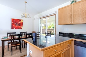 A modern kitchen with a black countertop, wooden cabinets, a dining area with chairs, and a red abstract painting on the wall. - Pukeawe Hale Family Home Near Hawaii Volcanoes National Park, Kitchen, WD, Lanai (Volcano)