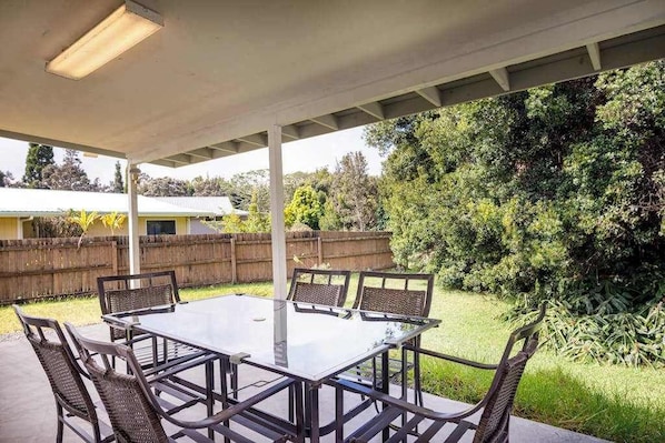 Eine Terrasse im Freien mit einem Tisch aus Glas und Korbstühlen, umgeben von einem Holzzaun und Pflanzen.