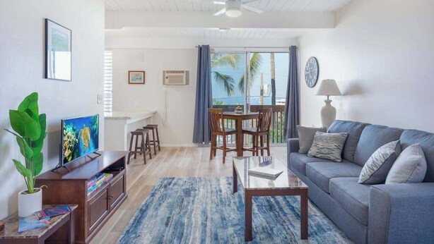 Een woonkamer met een bank, televisie, eettafel, stoelen en uitzicht op de oceaan.