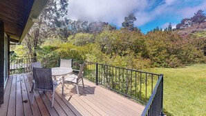 A wooden deck with outdoor furniture, surrounded by a metal railing, overlooking a lush garden and trees. - New Fall $pecial Nearly Two Rainforest Acres by Volcanoes National Park (Volcano)