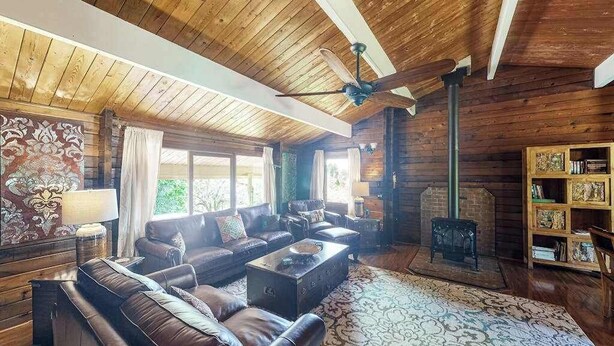 A log cabin interior with a wooden ceiling, leather sofas, a fireplace, and a bookshelf. - New Fall $pecial Nearly Two Rainforest Acres by Volcanoes National Park (Volcano)
