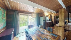 A rustic cabin interior with a wooden dining table, kitchen area, and large windows. - New Fall $pecial Nearly Two Rainforest Acres by Volcanoes National Park (Volcano)