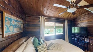 A wooden cabin room with a bed, a ceiling fan, a television, and a window. - New Fall $pecial Nearly Two Rainforest Acres by Volcanoes National Park (Volcano)