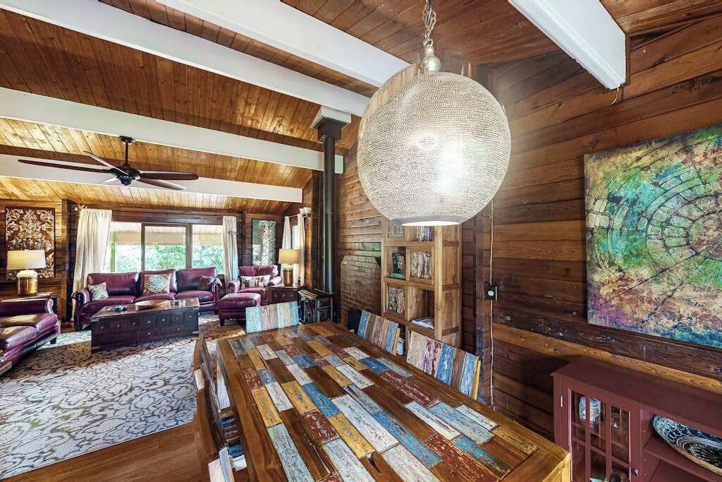 A spacious room with a large wooden dining table, a ceiling fan, and a hanging light fixture.