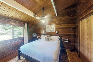 A wooden cabin bedroom with a bed, ceiling fan, and a window. - New Fall $pecial Nearly Two Rainforest Acres by Volcanoes National Park (Volcano)