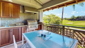 Eine Küche mit Holzschränken, einem Grill und einem Glastisch mit Blick auf einen Golfplatz.