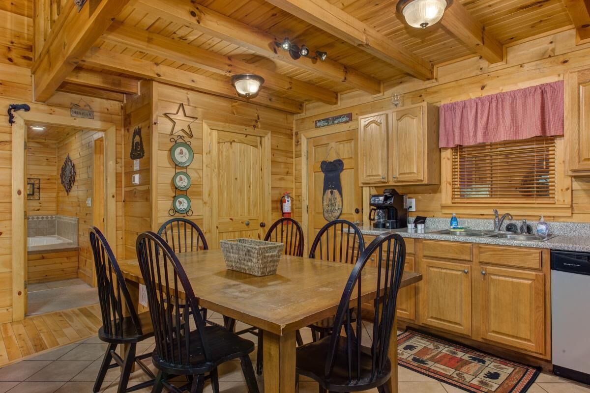 A wooden cabin interior with a dining table, chairs, a kitchen area, and a fireplace.