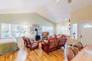 A spacious living room with a sofa, chairs, a fireplace, and large windows. - Volcanoes National Park Forest Retreat with Kitchen + Laundry-Near Shops/Cafe's (Volcano)