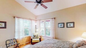 Ein Schlafzimmer mit Bett, Stuhl, Schreibtisch, Deckenventilator und zwei blickdichten Fenstern.
