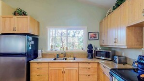 Eine Küche mit Holzschränken, einem Kühlschrank, einer Mikrowelle, einem Toaster und einem Fenster mit Blick auf Bäume.