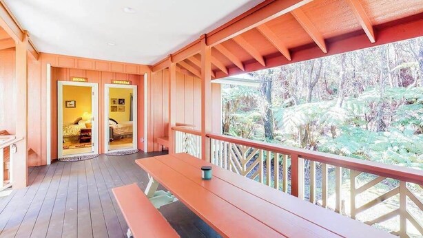 Eine Holzterrasse mit einer Bank, Blick auf einen Wald und zwei Türen, die zu Zimmern führen.