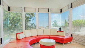 Ein modernes Wohnzimmer mit einem roten Ecksofa, einem Glastisch und großen Fenstern mit Jalousien.