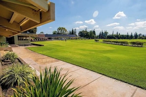 Ein Golfplatz mit blauem Himmel, ein Gebäude mit Überdachung und einem gepflegten Rasen.