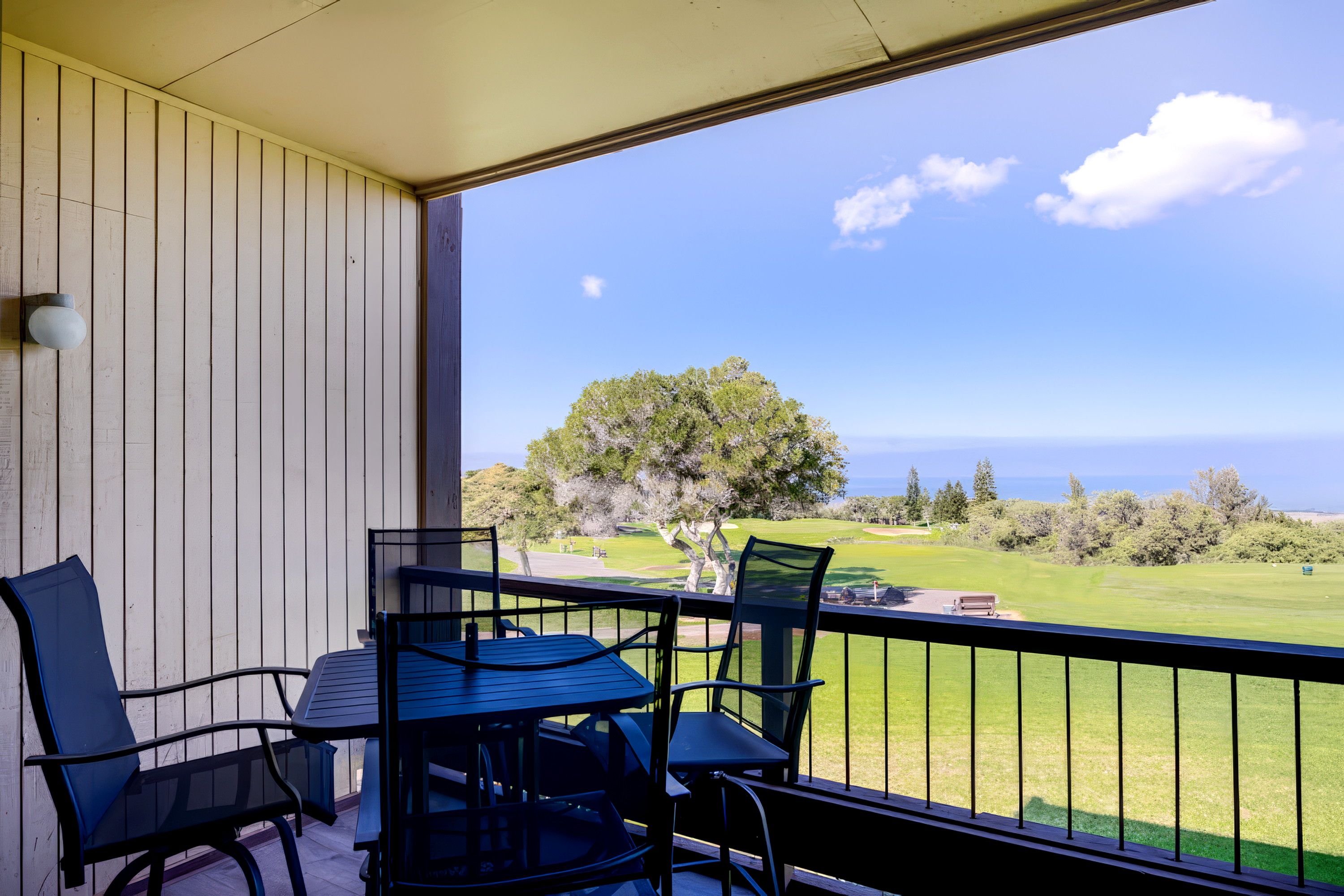 Un balcon avec une table et des chaises, donnant sur un terrain de golf et l’océan.