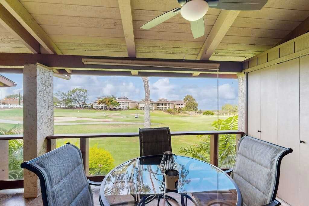 A covered outdoor seating area with a table and chairs, a ceiling fan, and a view of a golf course.