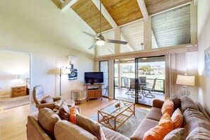 A spacious living room with a ceiling fan, a television, and a view of the outdoors through large sliding glass doors.