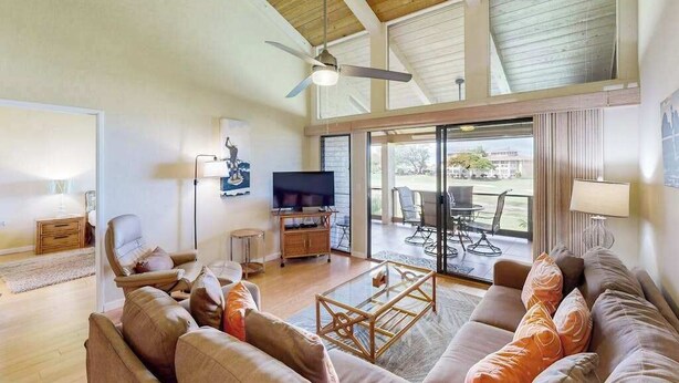 Ein geräumiges Wohnzimmer mit Deckenventilator, Fernseher und großem Fenster mit Blick auf einen Balkon.