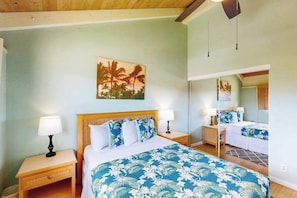 A hotel room with a bed, two bedside tables with lamps, a large mirror, and a tropical-themed painting on the wall. - *New* Ocean and Fairway Views from a Waikoloa Villa (Waikoloa Village)