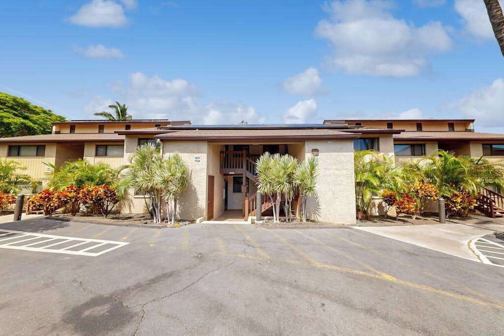 A hotel with a central entrance, a parking lot, and surrounding landscaping.