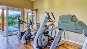Ein Fitnessraum mit Cardiogeräten, einem Spiegel und Blick auf Grünflächen.