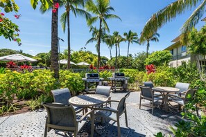 An outdoor patio with seating, a grill, and lush tropical vegetation. - Waikoloa Beach/Golf Resort Villa- Pool, Hot Tub, AC, Kitchen, Walk to Shops/Dine (Waikoloa)