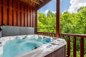 A hot tub on a wooden deck with a view of lush greenery. - Bear Essentials Lodge (Sevierville)