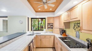 Uma cozinha moderna com armários de madeira, bancada preta, fogão e ventilador de teto.