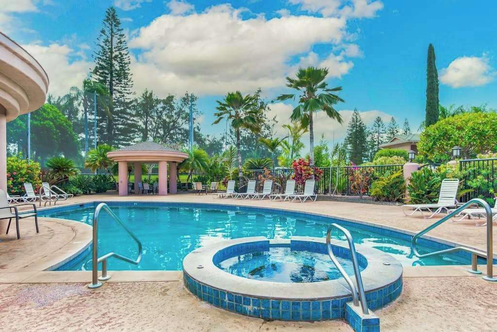 Una piscina con sillas de descanso y un jacuzzi, rodeada de palmeras y un pabellón.