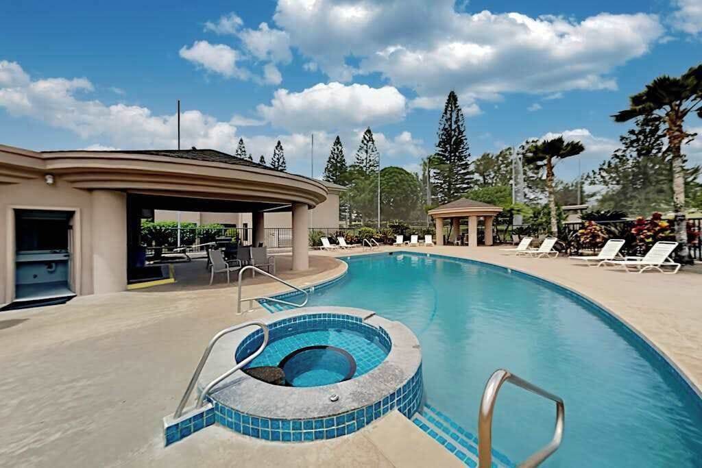 A swimming pool with a hot tub, lounge chairs, and a covered area.