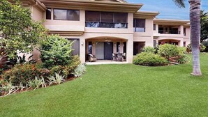 Una casa de dos pisos con un porche cubierto, rodeada de jardines cuidados y una palmera.