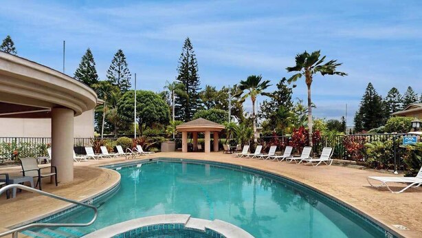 Una piscina con sillas de descanso, un pabellón y vegetación tropical.