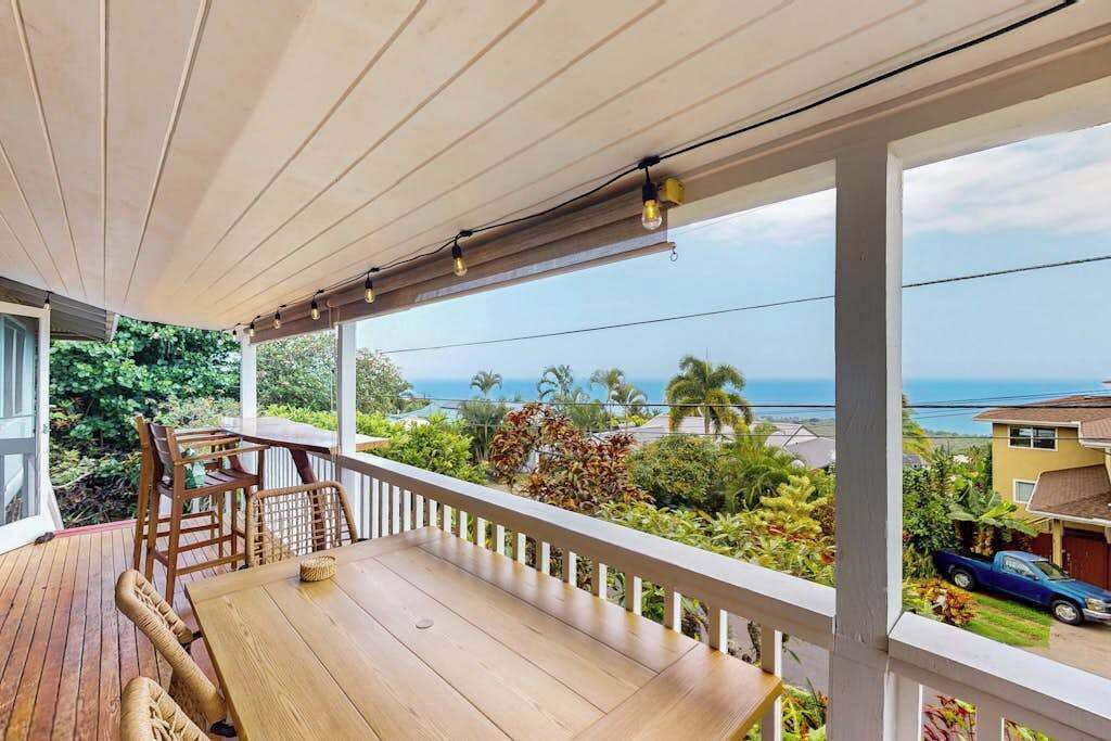 A wooden deck with a table and chairs, overlooking a residential area and the ocean.